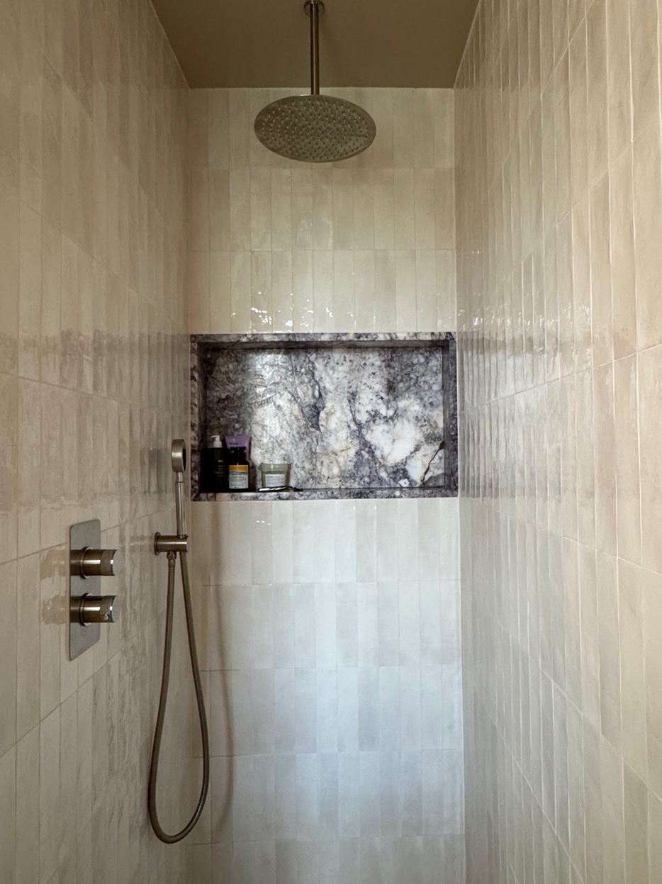 Shower with pale herringbone marble tiles, built-in niche, and brass overhead rose
