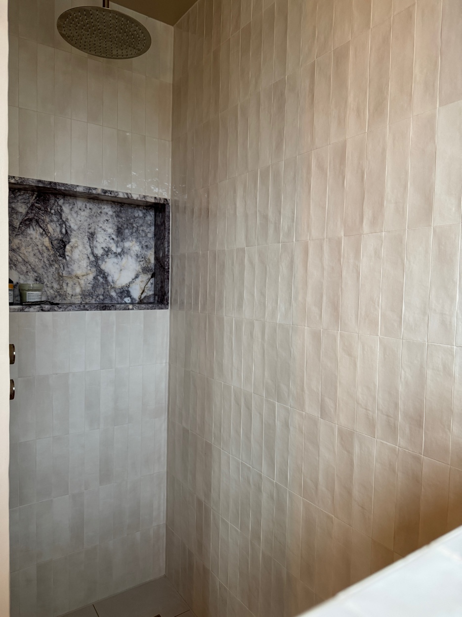 Wide view of the shower area showing the full herringbone marble tiling