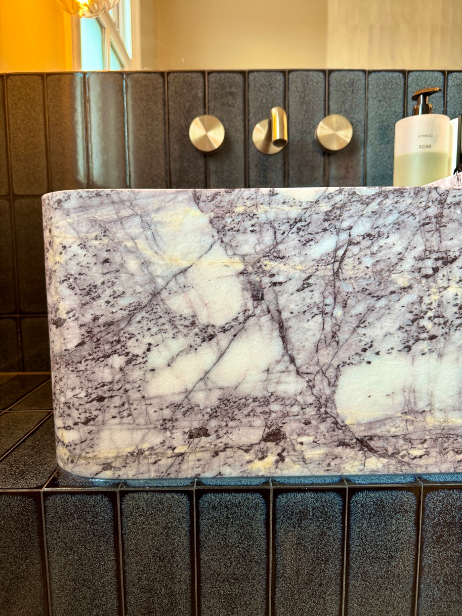 Close-up of purple-veined marble basin with brushed brass wall-mounted taps