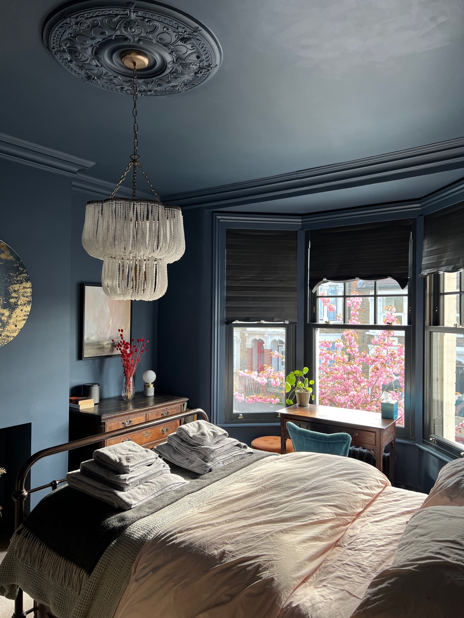 Blue bedroom with every surface painted inky blue, crystal chandelier, and cherry blossom outside the bay window