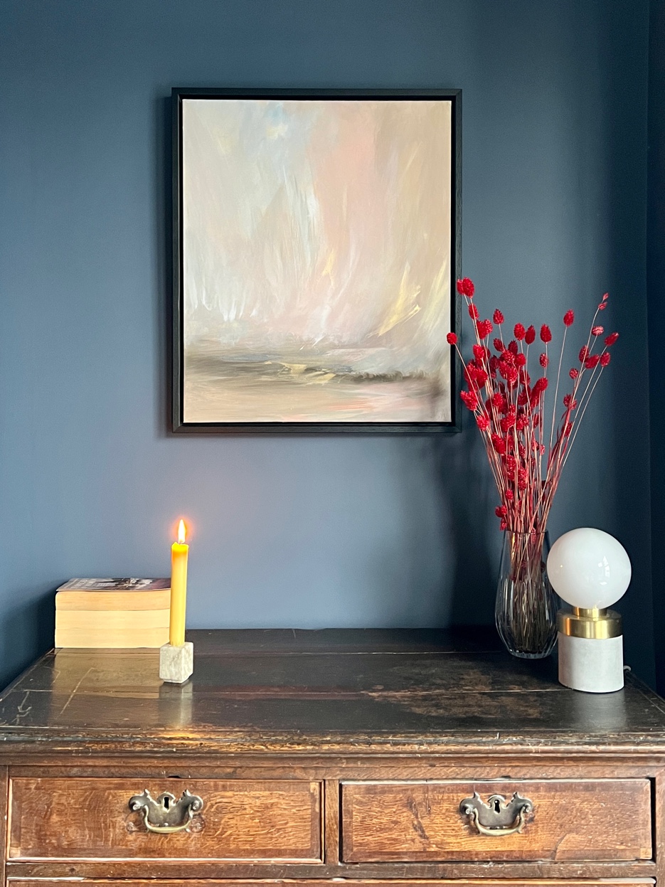 Detail of antique dresser in blue bedroom with landscape painting, candle, and red dried flowers