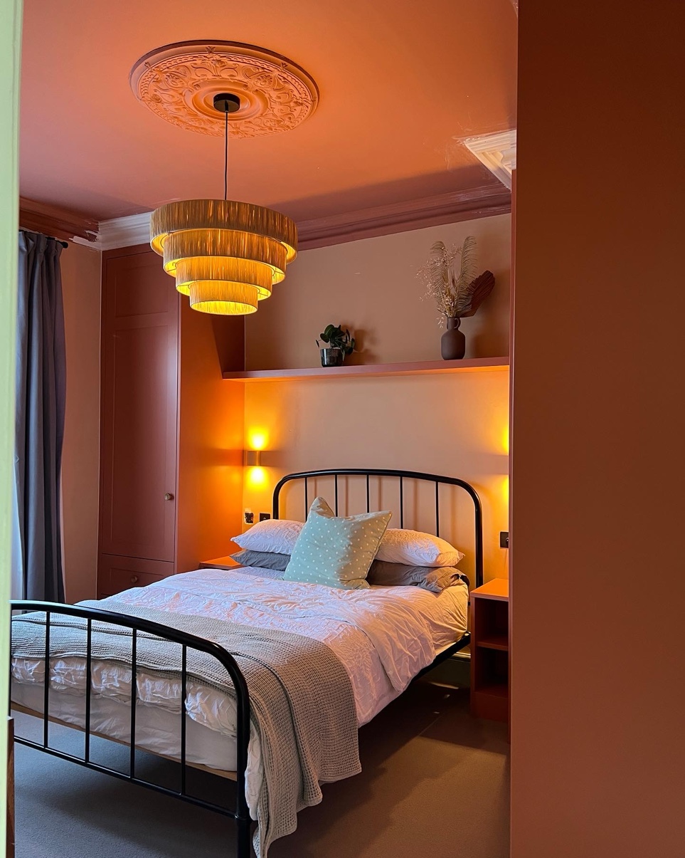 Terracotta bedroom at night viewed through the doorway, warm ambient lighting and rattan pendant light glowing