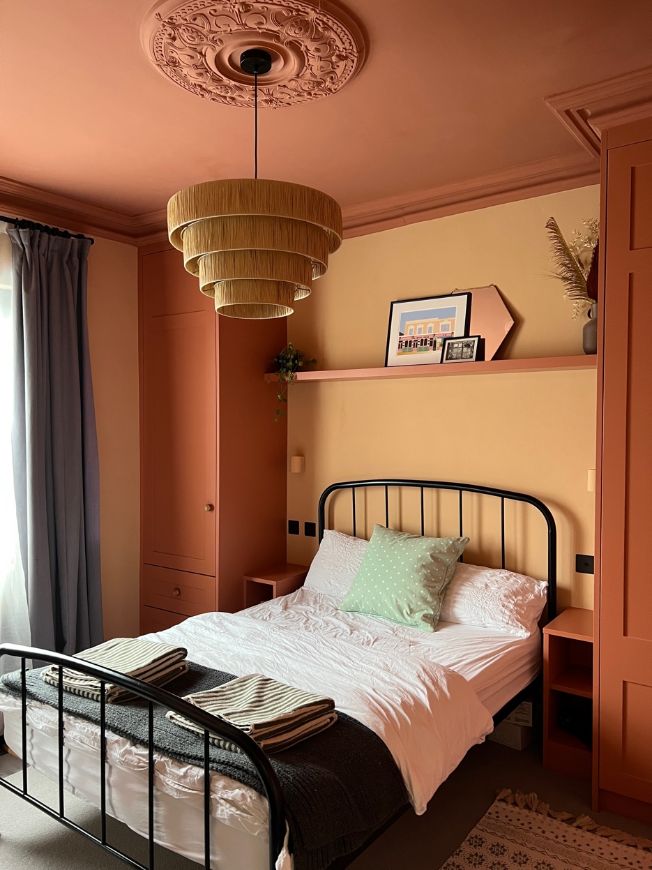 Terracotta bedroom with lacquered ceiling, rattan pendant light, iron bed frame, and built-in bookshelves in warm daylight