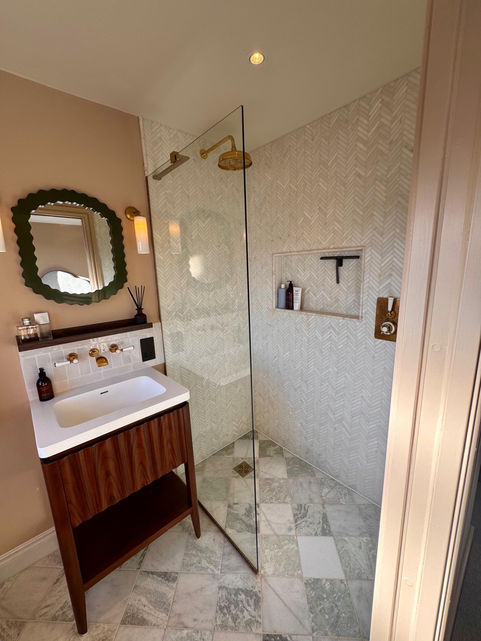 En-suite bathroom with green scalloped mirror, walnut vanity, and herringbone marble shower tiles