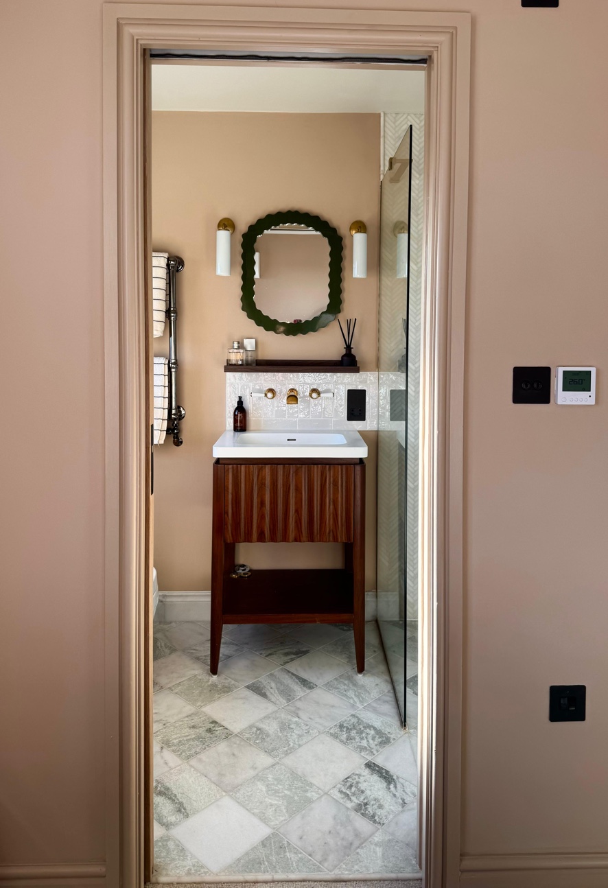 En-suite viewed through the doorway showing walnut vanity, green mirror, and marble floor
